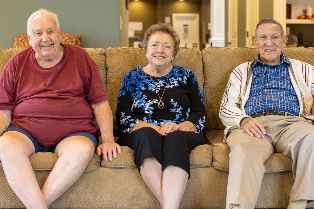 Three senior residents smiling while sitting on a couch